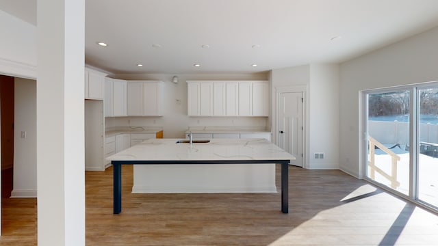 kitchen with light stone countertops, light hardwood / wood-style flooring, a kitchen island with sink, and a breakfast bar area