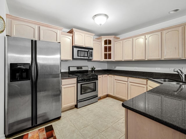 kitchen with appliances with stainless steel finishes, light brown cabinetry, dark stone counters, sink, and light tile patterned flooring