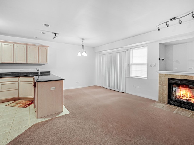 kitchen featuring sink, decorative light fixtures, a tiled fireplace, light carpet, and light brown cabinetry