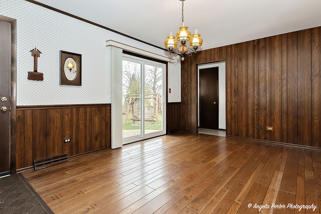 interior space featuring wooden walls, crown molding, wood-type flooring, and a notable chandelier