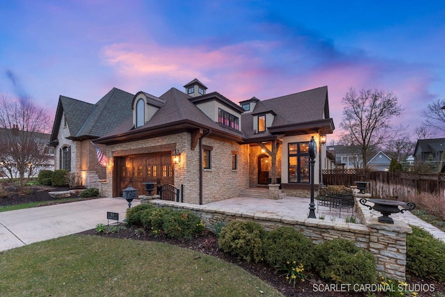 view of front of property with an attached garage, stone siding, fence, and concrete driveway