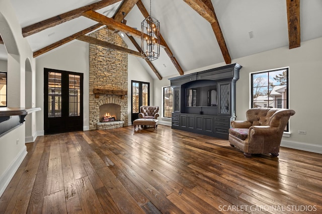 living area featuring an inviting chandelier, dark wood-type flooring, a stone fireplace, high vaulted ceiling, and baseboards