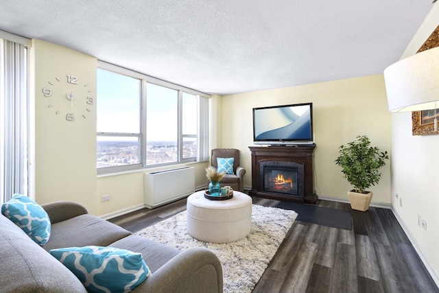 living room with a textured ceiling, dark wood-type flooring, a glass covered fireplace, and baseboards