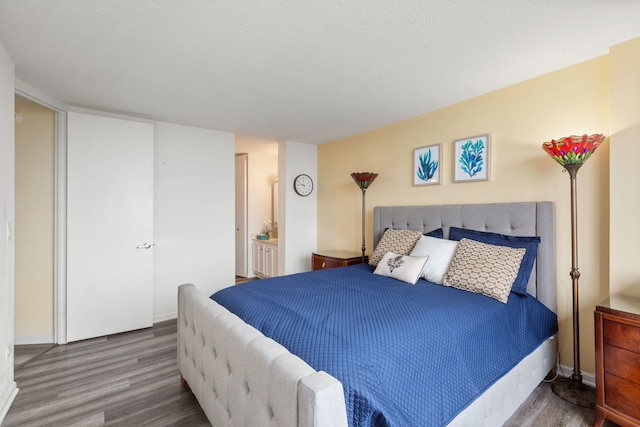 bedroom featuring ensuite bath, a textured ceiling, baseboards, and wood finished floors