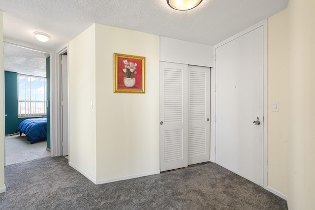 hall with dark colored carpet, a textured ceiling, and baseboards