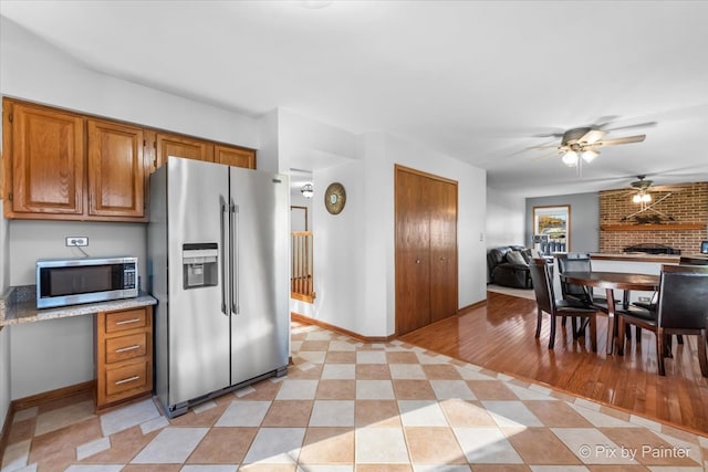 kitchen featuring appliances with stainless steel finishes, light hardwood / wood-style floors, a brick fireplace, and ceiling fan