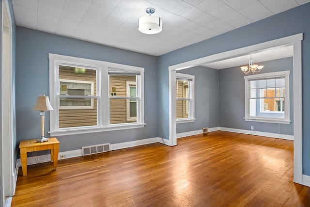 spare room featuring wood-type flooring and a notable chandelier