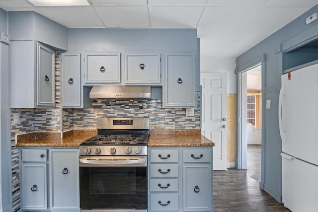 kitchen with a paneled ceiling, extractor fan, white refrigerator, dark stone countertops, and stainless steel range with gas cooktop