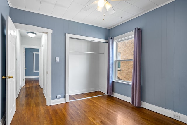 unfurnished bedroom featuring ceiling fan, wood-type flooring, wooden walls, and a closet