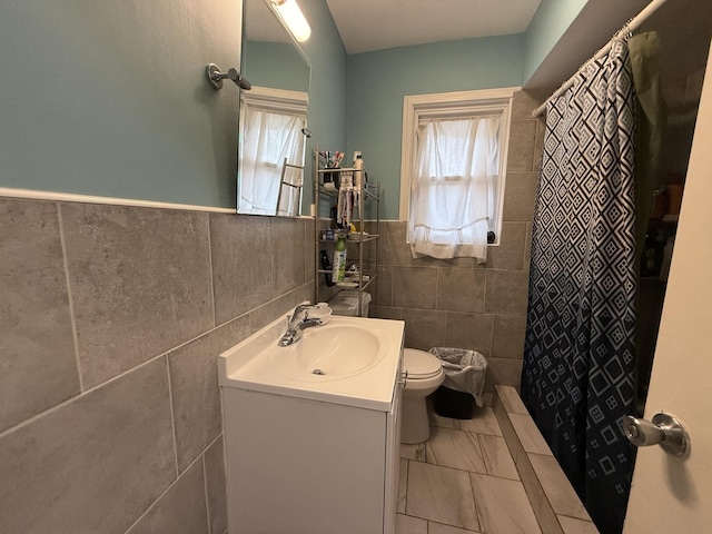 bathroom with a shower with shower curtain, vanity, toilet, and tile walls