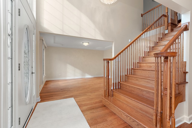 foyer entrance featuring a towering ceiling, wood-type flooring, and an inviting chandelier