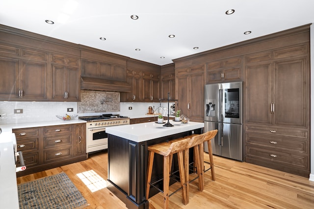 kitchen with stainless steel refrigerator with ice dispenser, light hardwood / wood-style flooring, a kitchen breakfast bar, a kitchen island, and gas range oven