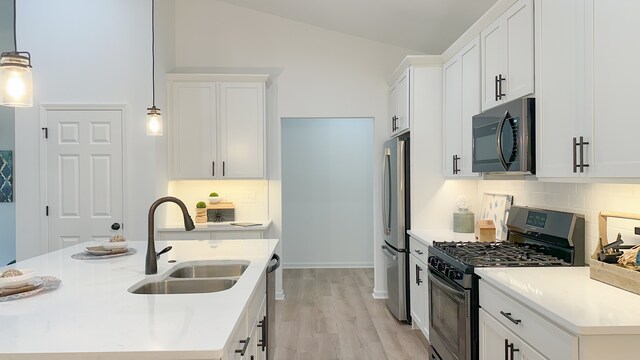 kitchen with stainless steel appliances, white cabinetry, sink, pendant lighting, and vaulted ceiling