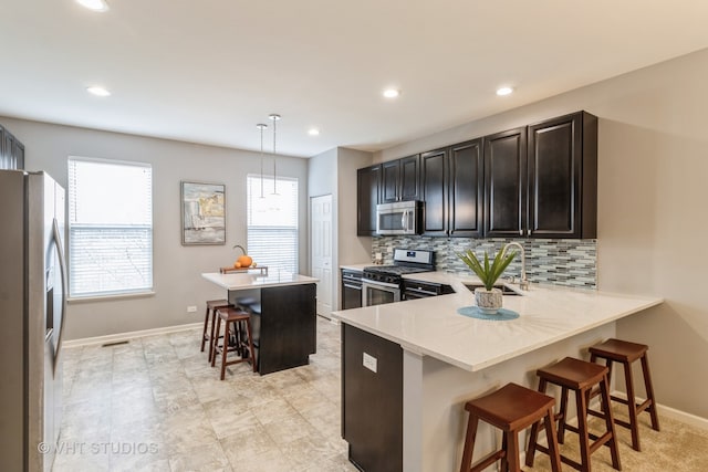 kitchen with a kitchen bar, appliances with stainless steel finishes, kitchen peninsula, sink, and pendant lighting