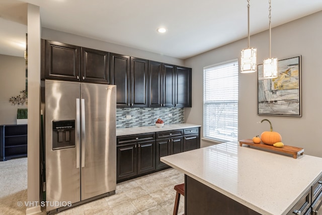 kitchen featuring backsplash, a healthy amount of sunlight, stainless steel refrigerator with ice dispenser, and hanging light fixtures