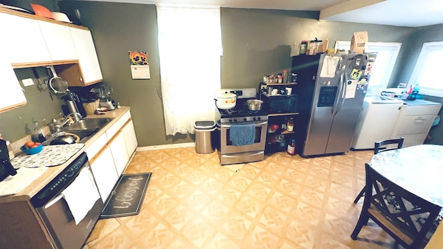 kitchen featuring beamed ceiling, sink, appliances with stainless steel finishes, washer and clothes dryer, and white cabinets