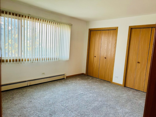 unfurnished bedroom with light colored carpet, multiple closets, and a baseboard heating unit