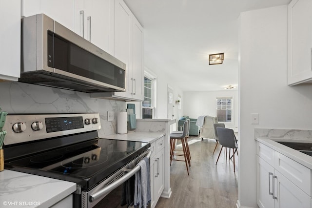 kitchen with backsplash, white cabinets, light hardwood / wood-style flooring, appliances with stainless steel finishes, and light stone counters