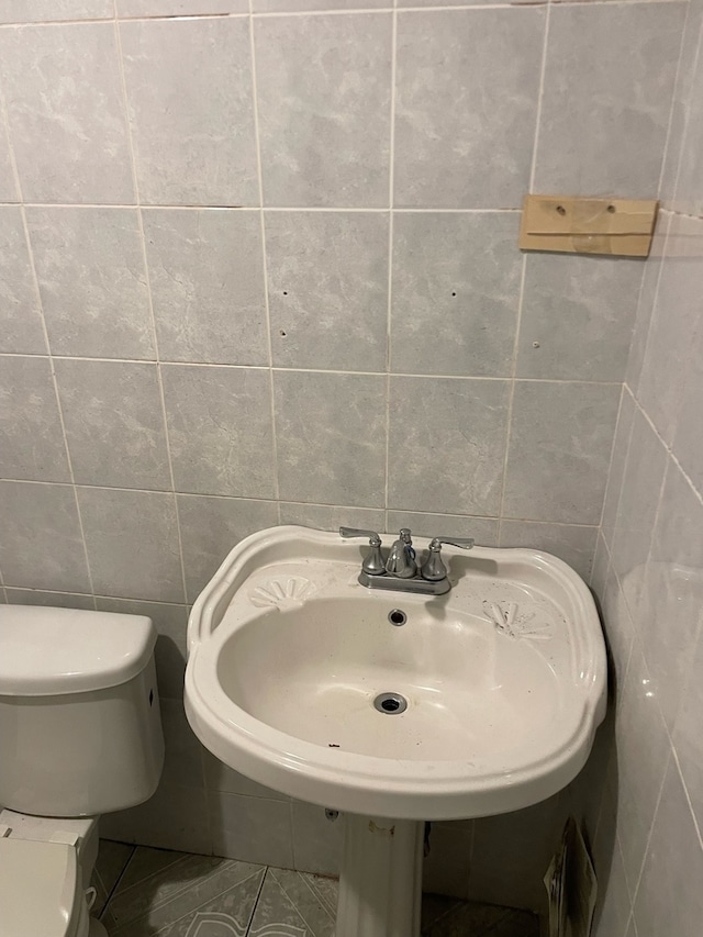 bathroom featuring toilet, tile walls, and sink