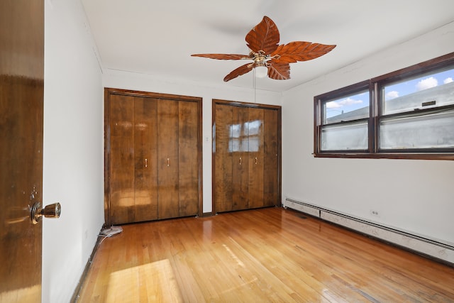 unfurnished bedroom featuring light hardwood / wood-style flooring, two closets, ceiling fan, and a baseboard radiator