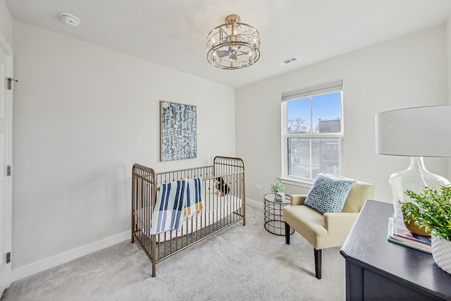 carpeted bedroom with a crib and an inviting chandelier