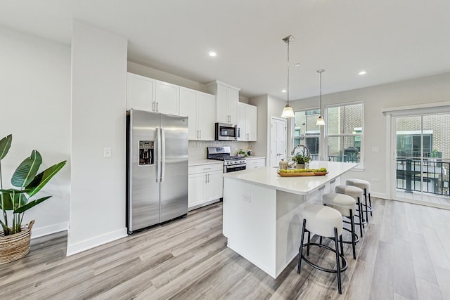 kitchen featuring pendant lighting, a kitchen island with sink, white cabinets, light hardwood / wood-style flooring, and appliances with stainless steel finishes