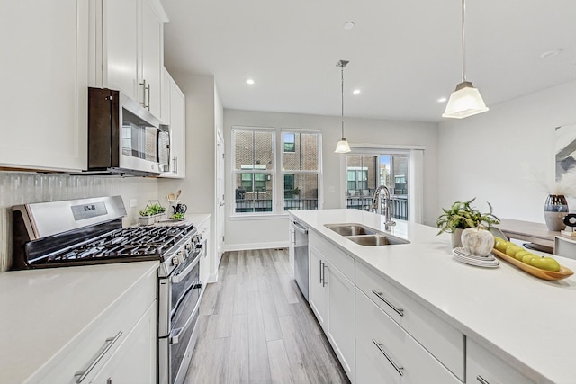 kitchen featuring sink, hanging light fixtures, appliances with stainless steel finishes, white cabinets, and light wood-type flooring