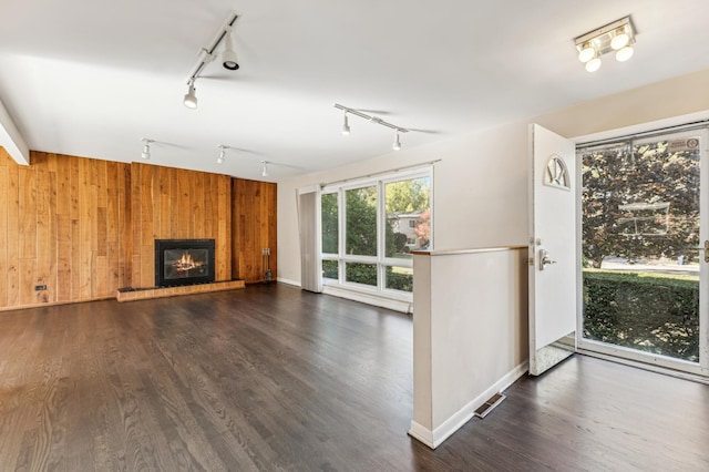 unfurnished living room with a glass covered fireplace, visible vents, wood finished floors, and wood walls