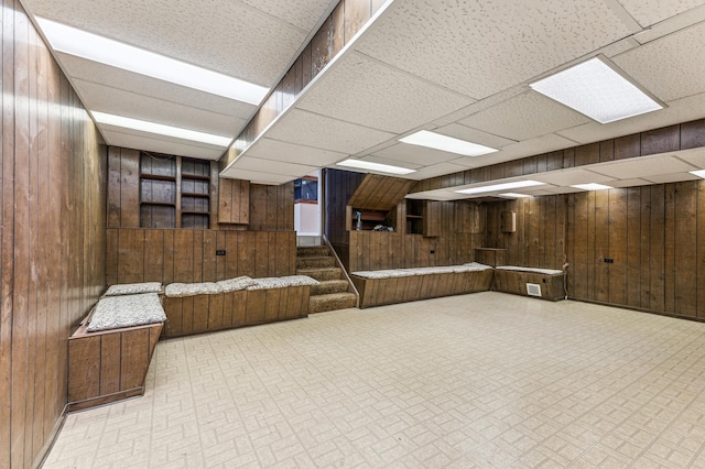 basement featuring wood walls and a drop ceiling