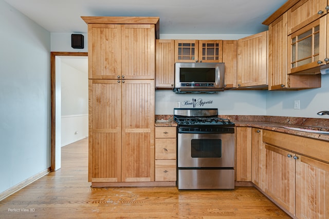 kitchen with dark stone counters, sink, light wood-type flooring, and appliances with stainless steel finishes