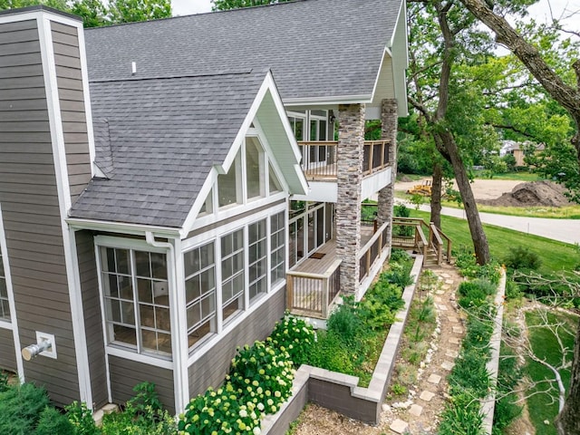 view of home's exterior with a deck, a chimney, a sunroom, and a shingled roof