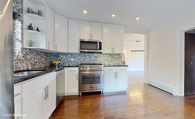 kitchen with appliances with stainless steel finishes, tasteful backsplash, wood-type flooring, white cabinets, and dark stone counters