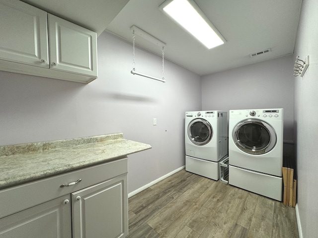 clothes washing area featuring cabinets, hardwood / wood-style flooring, and independent washer and dryer