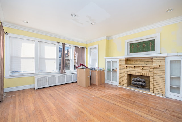 unfurnished living room featuring radiator, a brick fireplace, ornamental molding, and light wood-type flooring