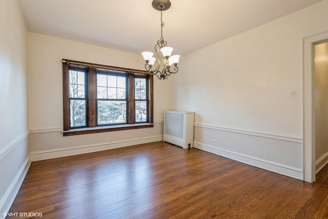 unfurnished room with dark hardwood / wood-style flooring, an inviting chandelier, and radiator heating unit