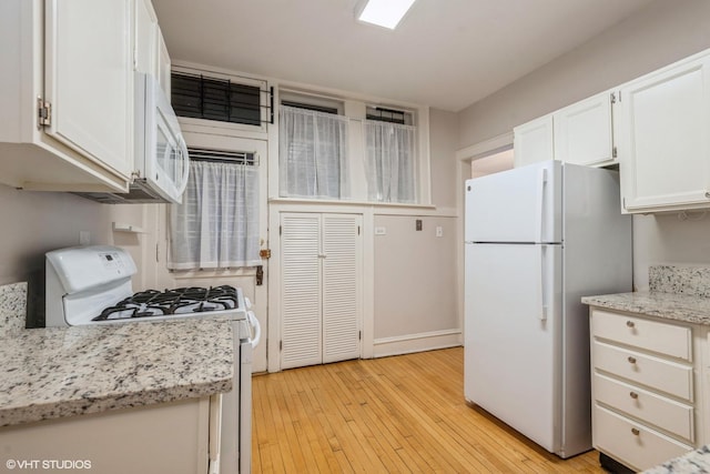 kitchen with light hardwood / wood-style floors, light stone countertops, white appliances, and white cabinetry