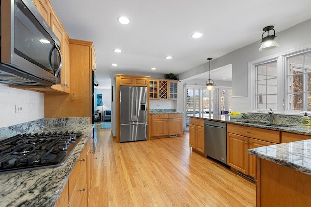 kitchen featuring sink, hanging light fixtures, light wood-type flooring, stone counters, and stainless steel appliances