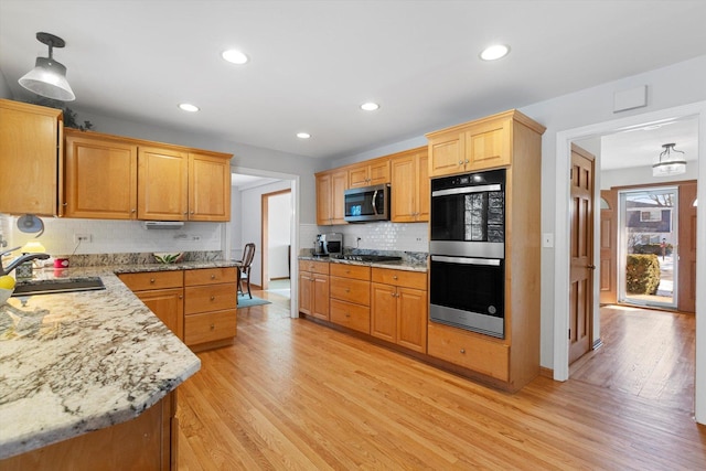 kitchen featuring sink, light hardwood / wood-style flooring, stainless steel appliances, tasteful backsplash, and decorative light fixtures