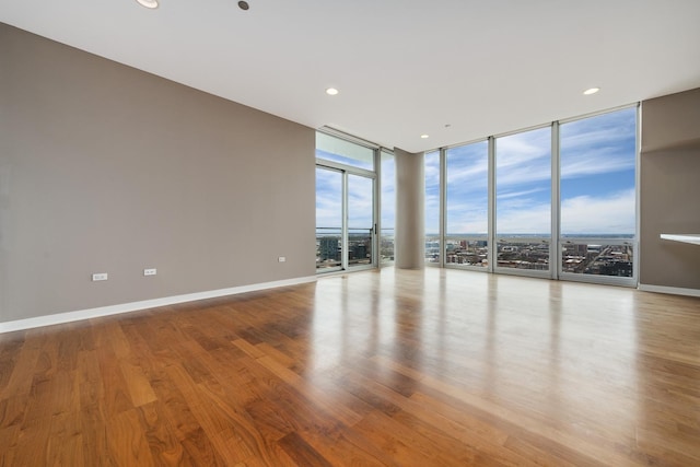 empty room with expansive windows, recessed lighting, baseboards, and wood finished floors