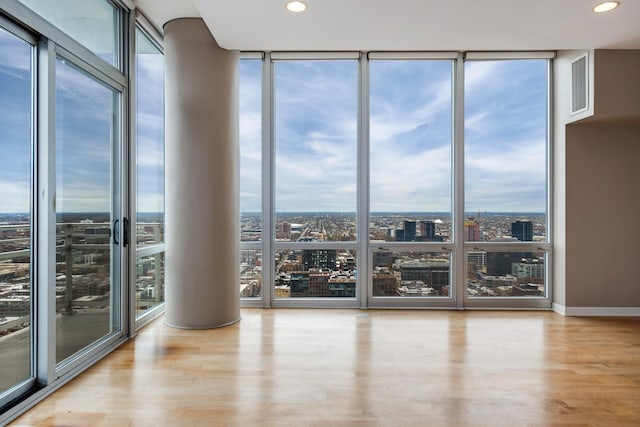 empty room with a view of city, a wall of windows, wood finished floors, and recessed lighting