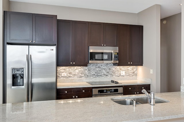 kitchen with backsplash, appliances with stainless steel finishes, a sink, dark brown cabinets, and light stone countertops