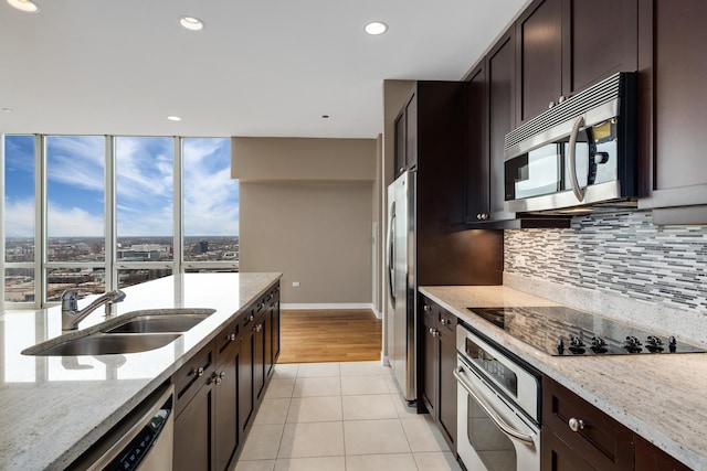 kitchen with stainless steel appliances, light stone counters, a sink, and decorative backsplash