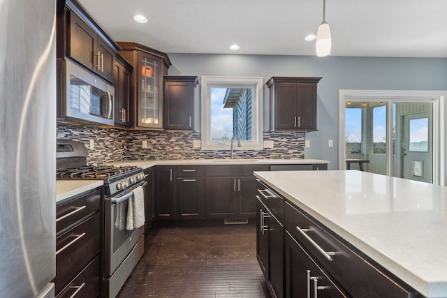 kitchen with dark brown cabinetry, tasteful backsplash, dark hardwood / wood-style floors, decorative light fixtures, and appliances with stainless steel finishes