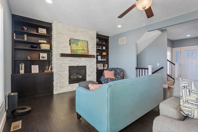 living room featuring a fireplace, built in shelves, dark hardwood / wood-style flooring, and ceiling fan