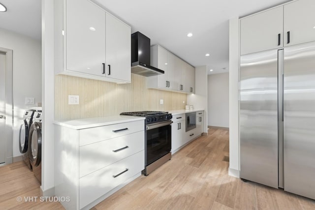 kitchen featuring white cabinets, built in appliances, light hardwood / wood-style floors, independent washer and dryer, and wall chimney exhaust hood