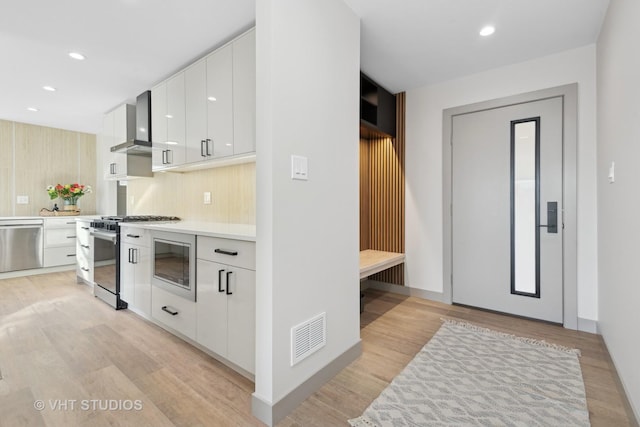 kitchen featuring white cabinetry, appliances with stainless steel finishes, light hardwood / wood-style floors, and wall chimney exhaust hood