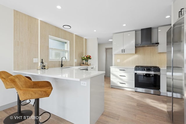 kitchen with white cabinetry, wall chimney range hood, kitchen peninsula, and appliances with stainless steel finishes