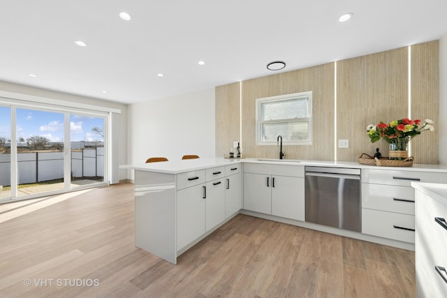 kitchen with sink, white cabinetry, stainless steel dishwasher, kitchen peninsula, and a wealth of natural light