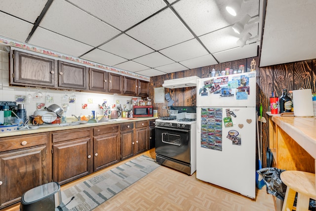 kitchen with wood walls, light parquet flooring, ventilation hood, white refrigerator, and black range with gas stovetop