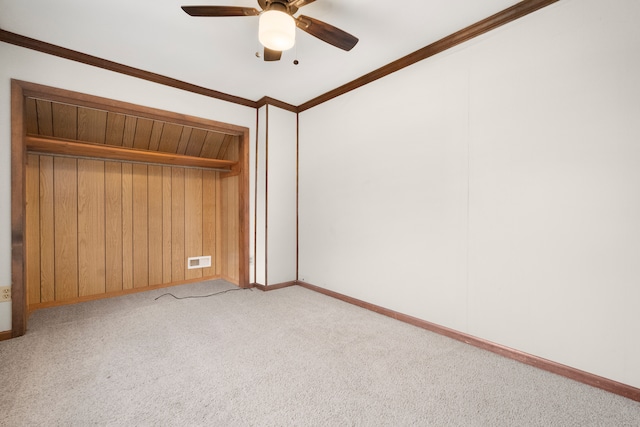 unfurnished bedroom with a closet, ornamental molding, wood walls, light colored carpet, and ceiling fan